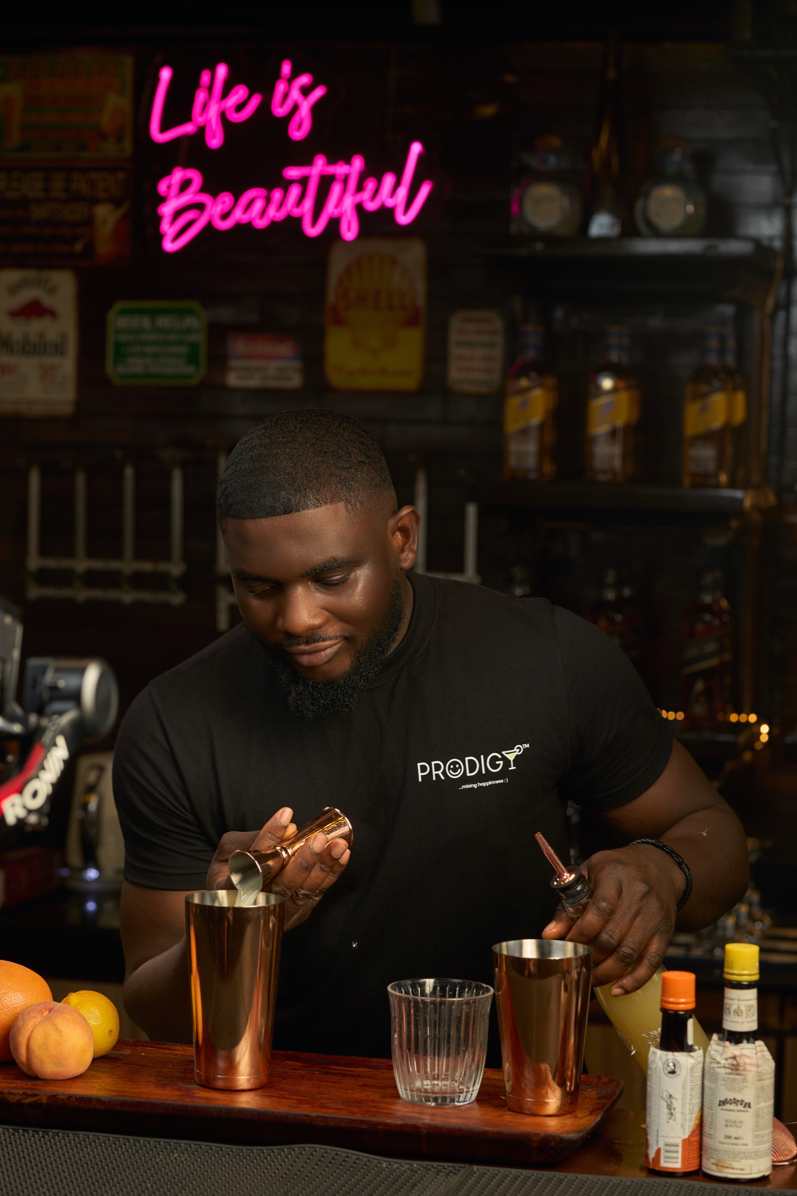 Prodigy mixing cocktails under a neon 'Life is Beautiful' sign